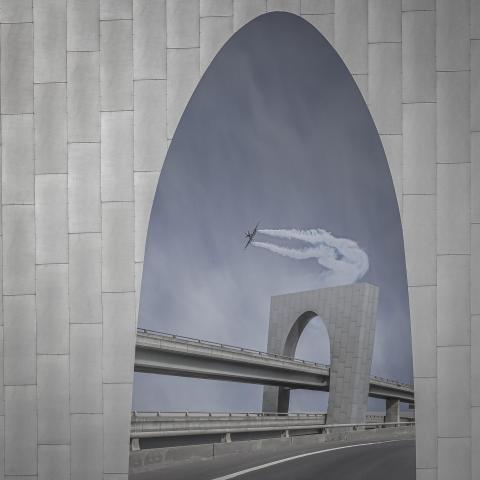 Archway leading to a bridge with an airplane flying through