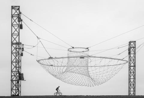 A large net hanging from tall towers, with a bike rider under neath